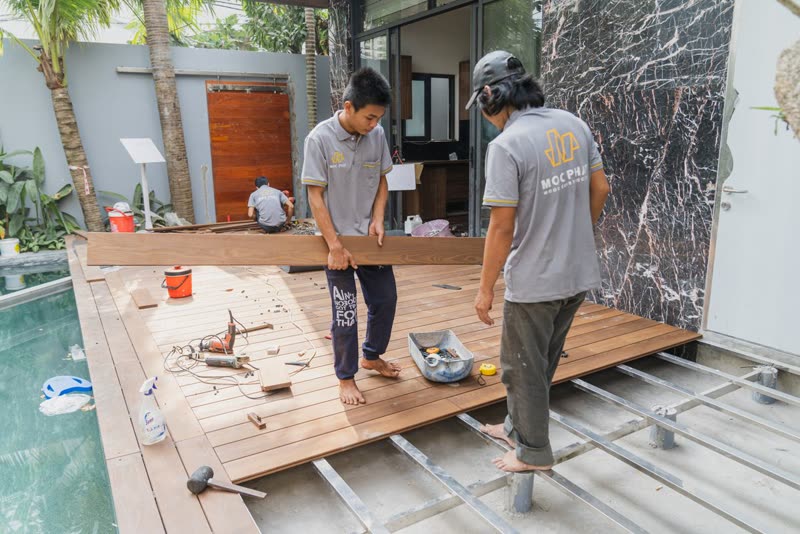 Two workers laying deck boards across the joists of a new deck
